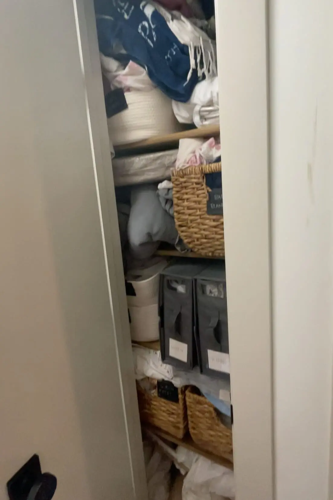 Disorganized linen closet overflowing with bedding, towels, and storage baskets before decluttering and reorganization.